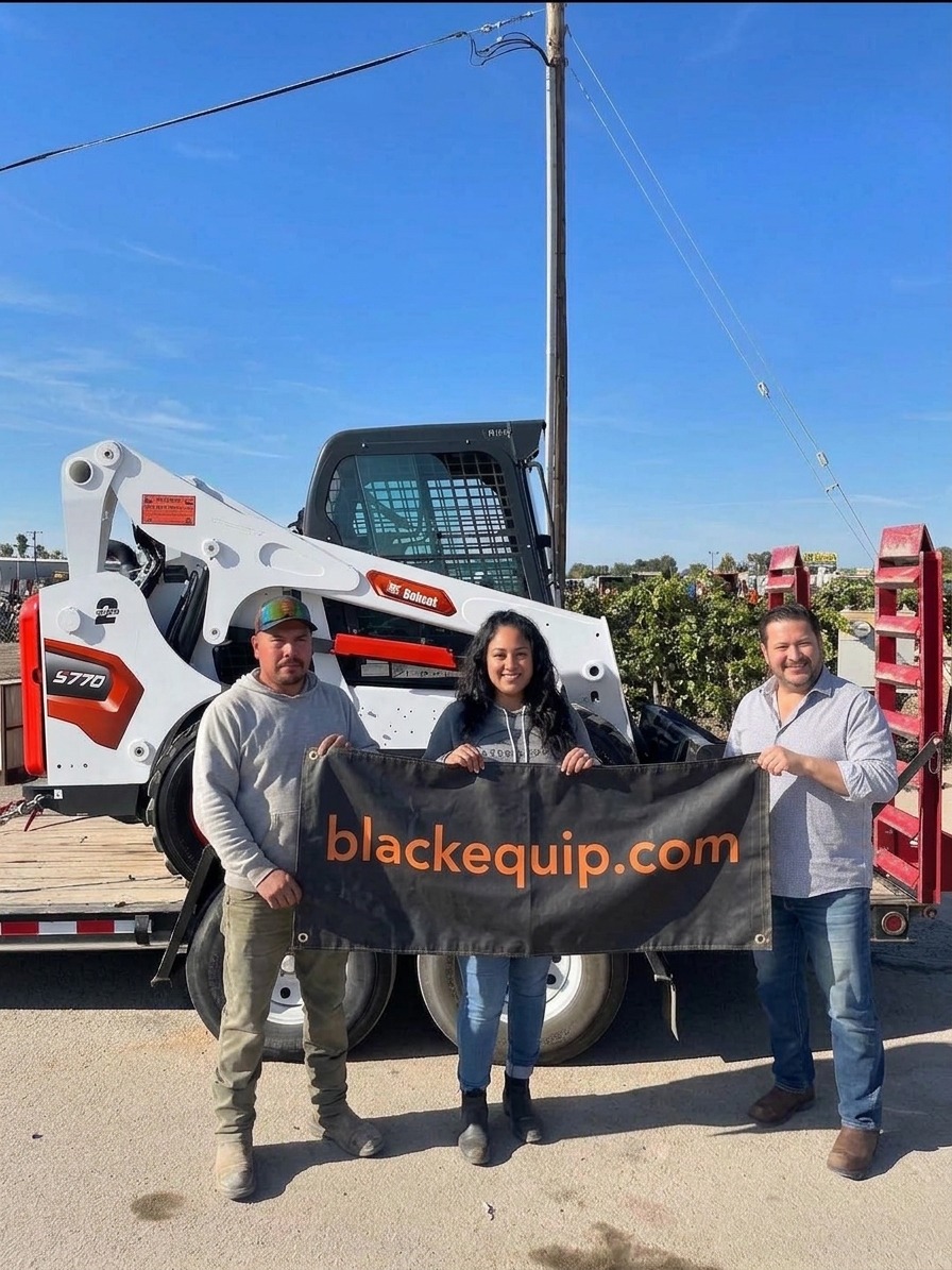 The Blackbull Equipment LLC team holding a blackequip.com banner in front of a Bobcat S770 skid steer loaded on a trailer